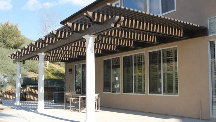 Decorative black and white lattice pergola over backyard patio with columns and dining area